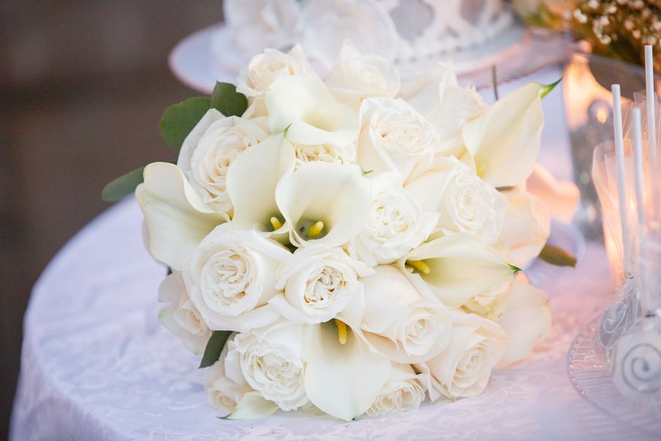 Close-up of an elegant white wedding bouquet with roses and lilies on a decorated table.
